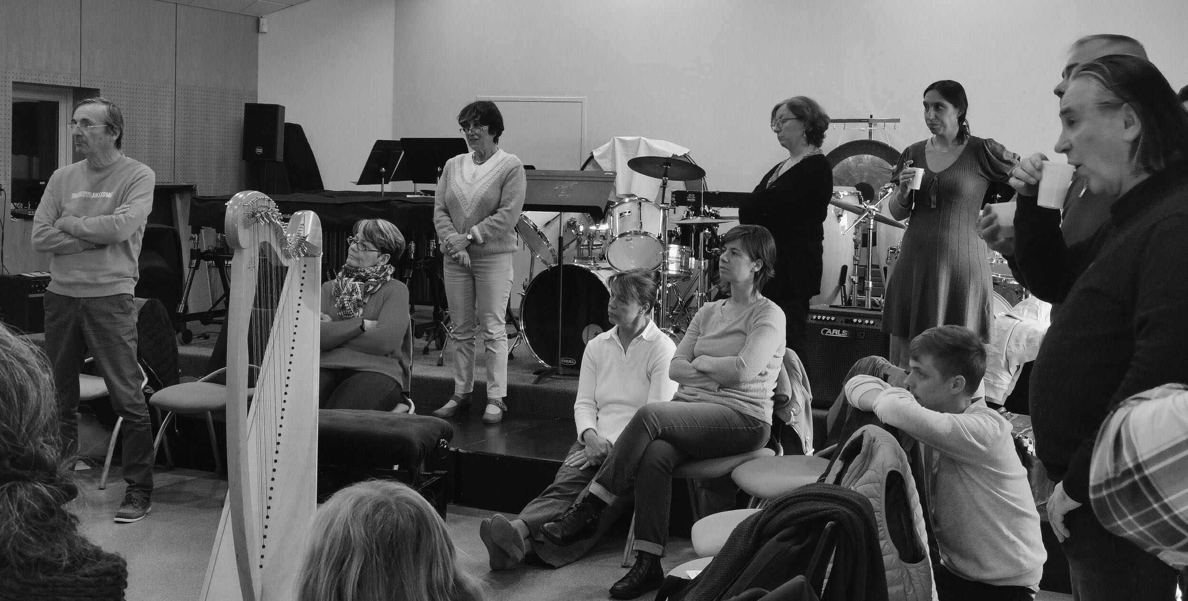 Atelier en salle de répétition : une harpiste joue, les autres musiciens écoutent debout et assis.