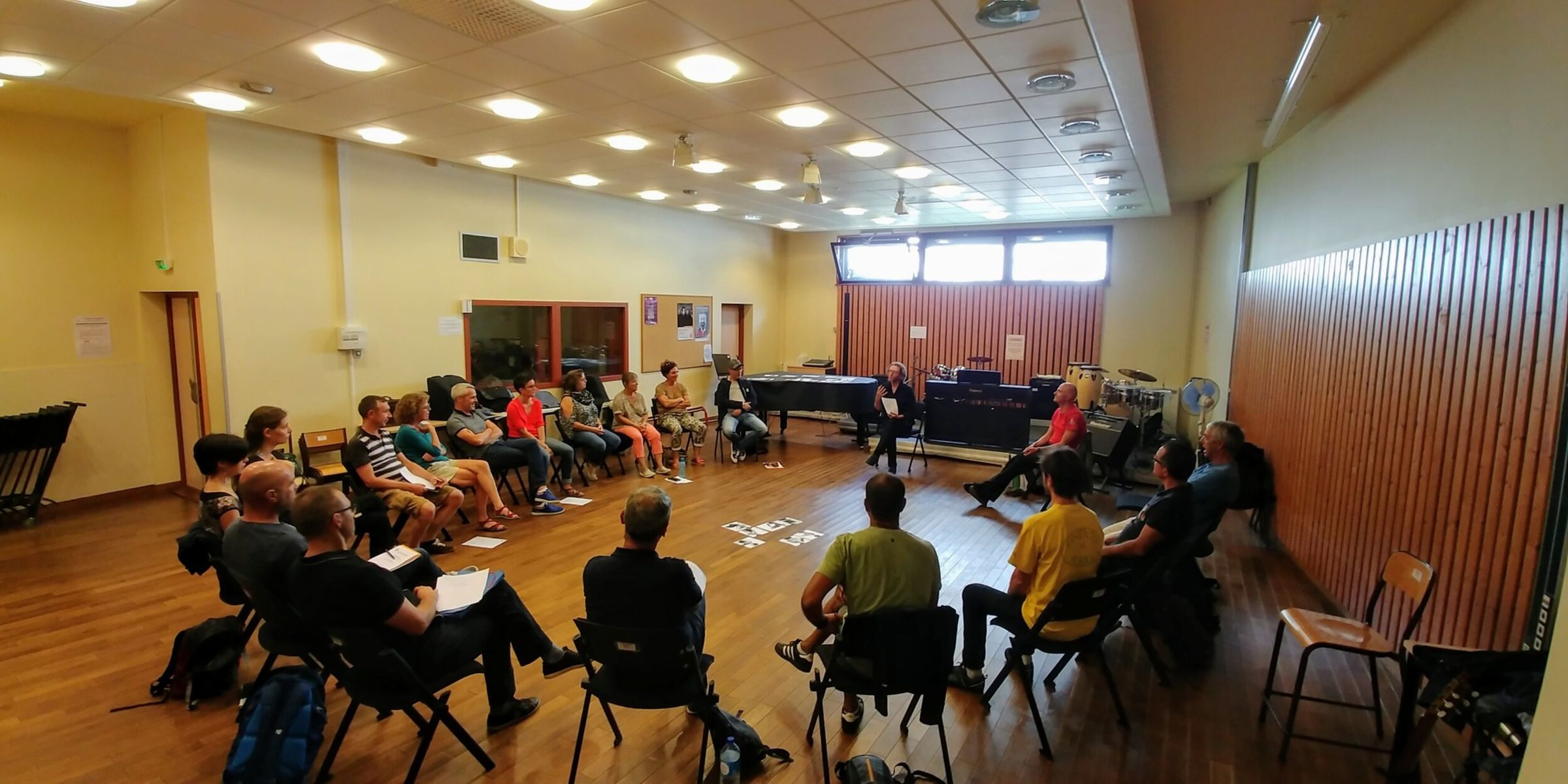 Une cinquantaine de musiciens assis en grand cercle dans une salle de répétition, pendant un atelier.