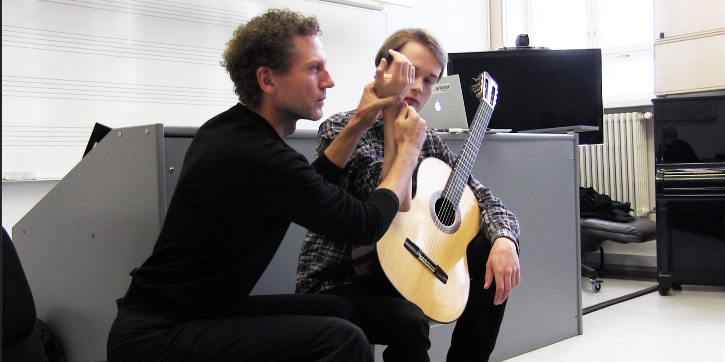 Marc Papillon, debout, guide le geste d’un jeune guitariste assis.